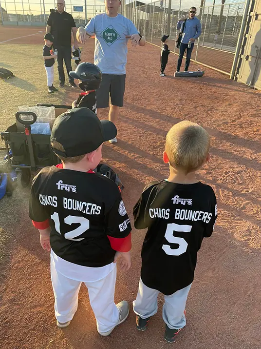 Two young boys playing baseball. Each has a jersey sponsored by Chaos Bouncers.